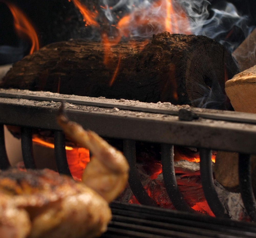 Argentinian style grill in use with chicken roasting and coals ignited