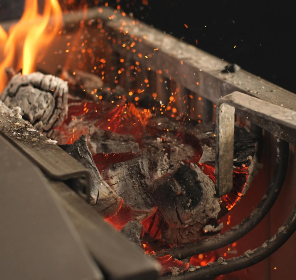 Up close shot of separate firebox in use on Argentinian style charcoal grill with fire poker stoking coals