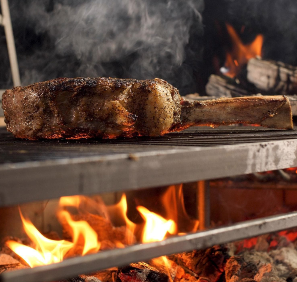 Large tomahawk steak being grilled over charcoal on Argentinian style gaucho grill
